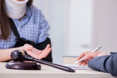 A blurred woman with a neck brace sits at a desk, meeting with a lawyer.