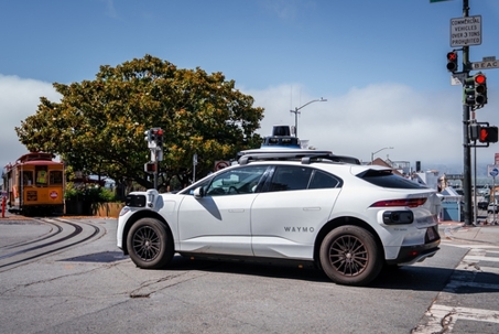 San Francisco, USA. July 4, 2025. A white Waymo SUV with lidar and sensors waits at a light by cable car tracks in San Francisco, near Hyde Street and Beach Street, in cool midday foggy light.