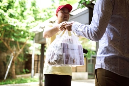 Delivery person hands a bag of takeout to a customer.