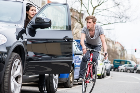 A woman opens a car door into the path of a cyclist